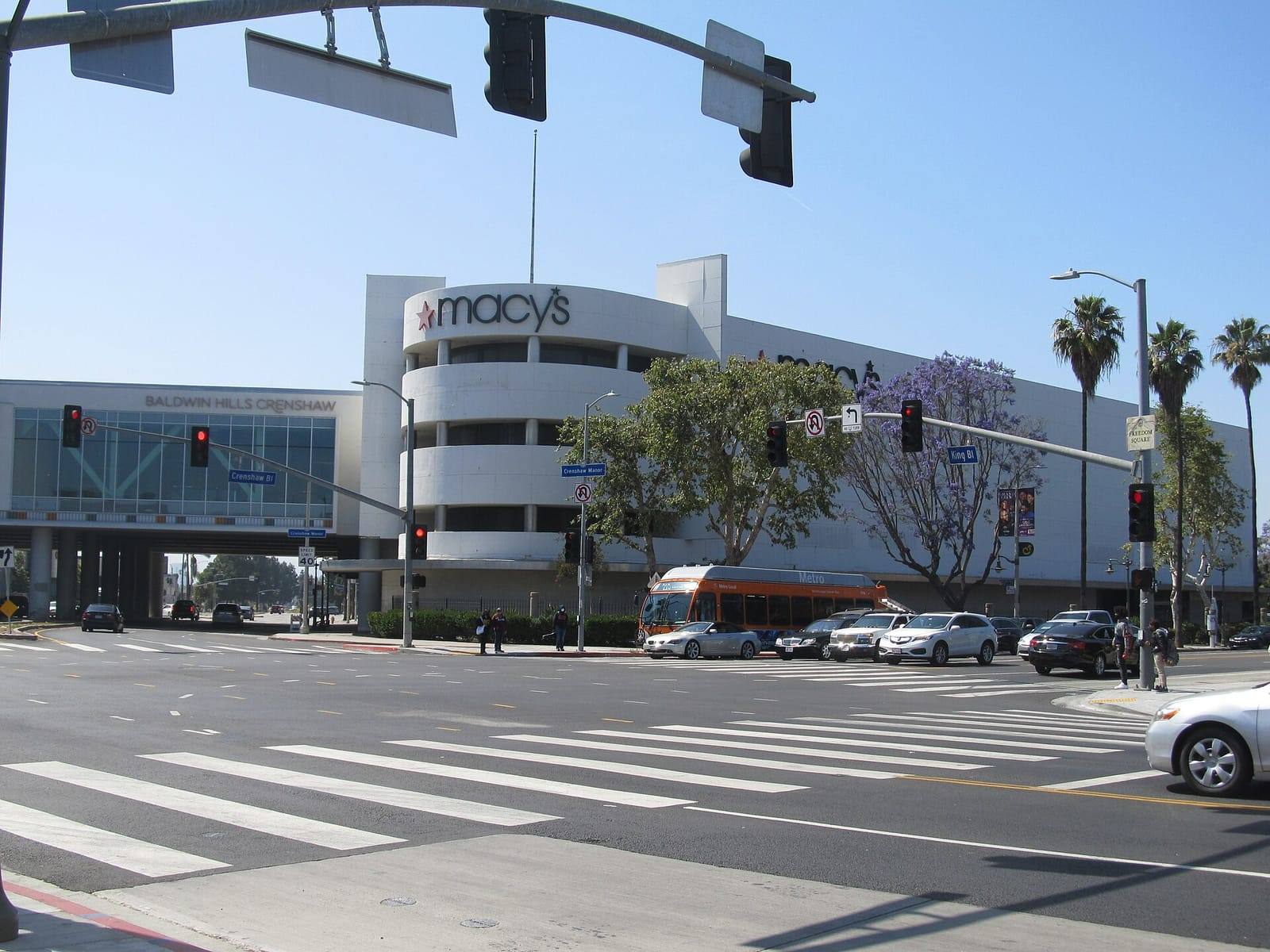 Baldwin Hills Crenshaw Plaza at the corner of Crenshaw Boulevard and Martin Luther King Jr. Boulevard, with a jacaranda tree in bloom and a Metro bus passing