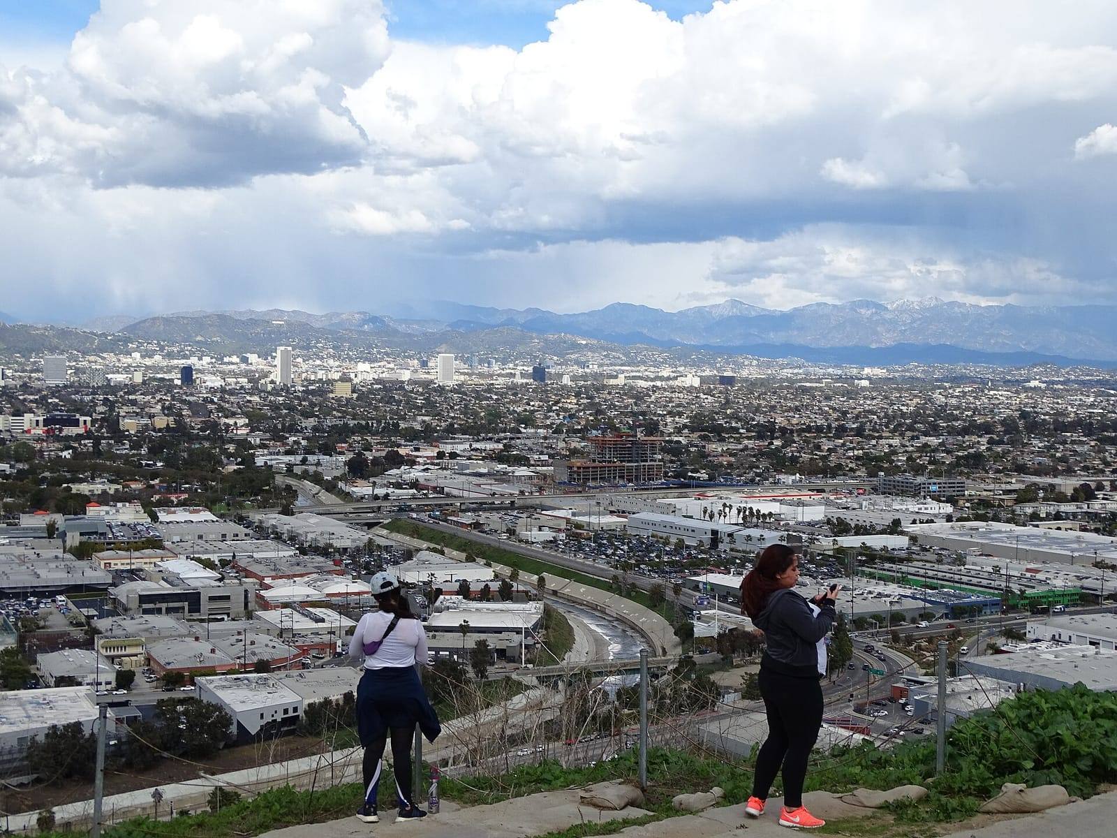 Two hikers look out from the Baldwin Hills over the Los Angeles Basin toward the Hollywood Hills and snow-capped San Gabriel Mountains